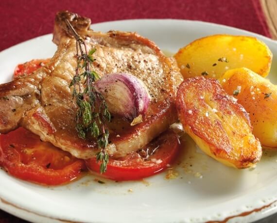 Koteletts vom Schwein an gebratenen Tomaten und mit Knoblauch und Thymian verfeinerter Kräuterbutter