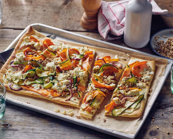 Helle Pizza mit Gemüse von Zucchini und Karotten an Feta mit karamelisierten Sonnenblumenkernen