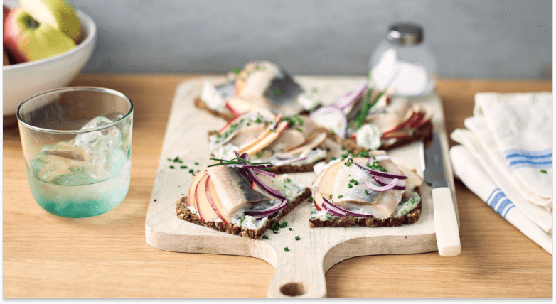 Smörrebröd mit Hering und Apfel auf Schneidebrett mit Messer