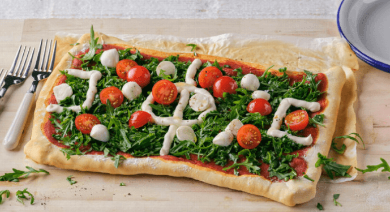 Pizza mit Rucola, Oliven, Tomaten und Mayonnaise als Fußballfeld